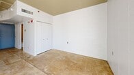 Located at 1 N Fifth Ave in downtown Tucson, Arizona, this studio unit offers an efficiently designed single-floor layout with an industrial aesthetic. The open living area features polished concrete floors and white-painted concrete block walls that lend a clean, urban character to the space. Exposed conduit along the ceiling adds to the industrial feel, while a sliding glass door floods the main area with natural light and provides views of the surrounding downtown cityscape.

The kitchen is positioned along one wall and includes a full suite of appliances — an electric range, dishwasher, and refrigerator — along with a single-basin sink, modest cabinetry with contemporary hardware, and open stainless steel shelving for additional storage. The counter space, though compact, is functional and well-organized.

A dedicated sleeping area features a double-door closet and the same concrete block wall construction, maintaining a cohesive aesthetic throughout the unit. The bathroom offers a clean, modern finish with a wall-mounted vanity, a mirrored medicine cabinet, and a combined bathtub and shower with tile surround. Concrete floors continue into the bathroom, tying together the overall design language of the space. This unit is well-suited for those seeking a minimalist, urban living environment in the heart of Tucson.