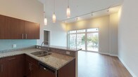 This contemporary single-floor residence is thoughtfully designed with an open-concept layout that seamlessly connects the kitchen, dining, and living areas. The kitchen serves as a central hub, featuring rich dark wood cabinetry, granite countertops, a glass tile backsplash, and a full suite of stainless steel appliances including a French door refrigerator, range, and built-in microwave. A peninsula with a double stainless steel sink and pendant lighting adds both functionality and style, while track lighting overhead ensures the space is well illuminated throughout.

The living area is anchored by expansive floor-to-ceiling windows and a sliding glass door that flood the room with natural light and frame views of the surrounding urban streetscape. Warm hardwood-style flooring flows through the main living spaces, creating a cohesive and inviting atmosphere.

The bedroom offers plush carpeting, a closet with built-in shelving, and a window that brings in soft, diffused light. Two bathrooms are finished with large-format tile flooring, granite-topped dark wood vanities, and clean, neutral tones. One bathroom includes a glass-enclosed walk-in shower with a ceiling-mounted fixture. A dedicated laundry room with a full-size washer and dryer adds everyday convenience to this well-appointed residence.