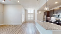 This well-appointed single-floor residence showcases a thoughtfully designed open-concept layout with modern finishes throughout. The living area is a standout, boasting dramatically high ceilings with clerestory windows that flood the space with natural light, complemented by light hardwood-style flooring that flows seamlessly through every room.

The kitchen is a functional centerpiece, featuring rich dark cabinetry that extends to the ceiling for ample storage, a herringbone tile backsplash, stainless steel appliances including a refrigerator, range, and built-in microwave, and a granite-topped peninsula with pendant lighting — ideal for both meal prep and casual dining.

The bedrooms are generously proportioned, each outfitted with ceiling fans, large windows with blinds for natural light and privacy, and the same warm hardwood-style flooring. The bathrooms are finished with granite-topped dark vanities, subway tile shower and tub surrounds, and brushed nickel hardware, creating a clean and cohesive aesthetic.

A central hallway connects the private areas of the home, with crisp white panel doors and recessed lighting adding to the polished, contemporary feel. The overall ambiance is bright, clean, and modern, with a neutral color palette that creates a welcoming and versatile living environment.