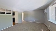 Located at 1422 N Glenwood Ave in Griffith, Indiana, this 2-bedroom, 1-bathroom apartment offers 720 square feet of single-floor living space. The living room features neutral gray walls, plush carpeting, baseboard heating, and windows that allow natural light to filter in, creating a comfortable common area. A pass-through window connects the living area to the kitchen, which is equipped with dark cabinetry, a black refrigerator, electric range, and hardwood-style vinyl flooring, providing a bold contrast to the lighter living spaces. The primary bedroom measures 180 square feet and includes carpeted floors, a window with tree-lined views, a wall-mounted AC unit, and baseboard heating. The second bedroom also features carpeting, a natural light window, and a built-in closet with double doors. A dedicated room with hardwood-style flooring and a ceiling fan serves as an additional flexible space. The bathroom includes a full tub-shower combo with tile accent walls and a clean white finish. A hallway with a closet rounds out this practical and well-organized floor plan, suitable for everyday residential living.