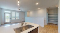 This well-designed residence offers a thoughtfully planned layout across its levels, connected by a carpeted staircase. The open-concept main living area is anchored by a modern kitchen featuring rich dark-stained cabinetry that extends to the ceiling, stainless steel appliances including a French door refrigerator, electric range, and built-in microwave. A central island with a white countertop and undermount stainless steel sink serves as a functional workspace, illuminated by stylish pendant lighting. Light wood-look flooring runs throughout the kitchen and living areas, complementing the neutral color palette.

The living space is airy and bright, with recessed lighting and a ceiling fan enhancing comfort. A half-wall partition elegantly defines the transition between the kitchen and the open living area. Bedrooms are carpeted for comfort, with large windows that frame lush outdoor greenery and invite ample natural light.

The bathrooms are finished with the same dark cabinetry, white countertops, and wood-look flooring. The primary bathroom features a dual-sink vanity with frameless mirrors and bright vanity lighting, while a secondary bathroom includes a single-sink vanity with access to a dedicated walk-in closet. Recessed lighting throughout ensures a bright and welcoming atmosphere across the entire space.