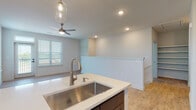 This well-designed residence offers a thoughtfully planned layout across its levels, connected by a carpeted staircase. The open-concept main living area is anchored by a modern kitchen featuring rich dark-stained cabinetry that extends to the ceiling, stainless steel appliances including a French door refrigerator, electric range, and built-in microwave. A central island with a white countertop and undermount stainless steel sink serves as a functional workspace, illuminated by stylish pendant lighting. Light wood-look flooring runs throughout the kitchen and living areas, complementing the neutral color palette.

The living space is airy and bright, with recessed lighting and a ceiling fan enhancing comfort. A half-wall partition elegantly defines the transition between the kitchen and the open living area. Bedrooms are carpeted for comfort, with large windows that frame lush outdoor greenery and invite ample natural light.

The bathrooms are finished with the same dark cabinetry, white countertops, and wood-look flooring. The primary bathroom features a dual-sink vanity with frameless mirrors and bright vanity lighting, while a secondary bathroom includes a single-sink vanity with access to a dedicated walk-in closet. Recessed lighting throughout ensures a bright and welcoming atmosphere across the entire space.