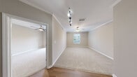 Located at 924 Timber Valley Way in Virginia Beach, Virginia, this single-floor residence offers a well-organized layout with a neutral color palette throughout, creating a clean and versatile living environment. The main living areas feature plush wall-to-wall carpeting, crown molding, and ceiling fans, lending a comfortable and polished feel. Track lighting accents select rooms, providing flexible illumination alongside natural light from windows fitted with blinds.

The kitchen is equipped with rich wood cabinetry, dark countertops, and black appliances including an electric range, over-the-range microwave, and refrigerator. Light wood-look flooring grounds the space and carries through into the bathroom, which features a full tub-shower combination, a toilet, and a vanity in a clean, bright setting.

The bedrooms are generously sized with soft carpeting, ceiling fans, and ample natural light. One room opens directly onto a private balcony through a sliding glass door, offering a pleasant outdoor view of surrounding greenery. A spacious walk-in closet with wire shelving provides practical storage. Additional rooms offer flexibility for use as bedrooms, a home office, or a den. The open-concept dollhouse view confirms a thoughtfully connected floor plan with easy flow between the kitchen, living, and bedroom areas.