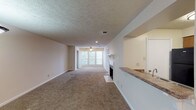 This single-floor residence at The Mansion offers a well-organized layout with a range of functional living spaces. The main living area is generously proportioned, featuring neutral-toned carpet, a textured ceiling, and a ceiling fan with integrated lighting. A fireplace serves as a focal point at one end, while a large window at the far wall allows natural light to fill the space. A half-wall with a granite-style countertop separates the living area from the kitchen, creating an open, connected feel.

The kitchen is equipped with warm oak cabinetry, granite-style countertops, and black appliances including a coil-top electric range with an overhead ventilation hood. Adjacent to the kitchen, a dining area features a pendant light fixture and access to the front entry door, with a nearby window providing additional natural light.

The bedrooms are carpeted and finished with neutral walls and textured ceilings. One bedroom includes a ceiling fan, a walk-in closet, and a window with blinds offering outside views. Additional bedrooms provide comfortable, versatile spaces with ample room.

The bathroom features tile flooring, a full-size soaking tub and shower combination, a wood-cabinet vanity with a granite-style countertop, and clean white fixtures, completing this straightforward and functional residence.