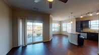This single-floor residence presents a thoughtfully designed open layout where the kitchen, dining, and living areas flow seamlessly together. Rich, dark hardwood flooring runs throughout the main living spaces, creating a cohesive and polished aesthetic. Crown molding accents the living room, which is equipped with a ceiling fan and connects directly to a private balcony through sliding glass doors, offering outdoor views and an abundance of natural light.

The kitchen is well-appointed with dark espresso cabinetry, granite countertops, a curved breakfast bar island, stainless steel appliances including a refrigerator, electric range, microwave, and dishwasher, and pendant lighting overhead. Track lighting and multiple windows with blinds further illuminate the space.

A hallway leads to the bedroom areas, one of which features plush carpeting and a large window with exterior views. The primary bathroom includes dark cabinetry with a white countertop vanity, a glass-enclosed shower, hardwood flooring, and direct access to a walk-in closet with built-in shelving. A secondary bathroom offers a similarly styled vanity with a large mirror. The overall ambiance is clean, modern, and move-in ready.