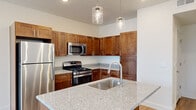 This thoughtfully designed single-floor residence offers a cohesive open-concept layout that seamlessly connects the kitchen, dining, and living areas. The kitchen is a standout feature, showcasing rich warm-toned cabinetry that extends to the ceiling, light speckled granite countertops, and a full suite of stainless steel appliances including a gas range, built-in microwave, and refrigerator. A central island with an undermount sink and stylish pendant lighting serves as both a functional workspace and a natural gathering point. Light hardwood-style flooring flows throughout the main living areas, lending warmth and continuity to the space. Large sliding glass doors open to a private balcony, filling the interior with natural light and providing outward views of the surrounding area. The bedroom offers plush carpeting, a window with outdoor views, and direct access to the rest of the unit. The bathroom is clean and functional, featuring a full tub-shower combination. Conveniently positioned nearby, a stacked washer and dryer unit adds practical in-unit laundry access. Recessed lighting and pendant fixtures throughout provide versatile illumination, while the neutral color palette creates a bright, move-in-ready atmosphere throughout the home.
