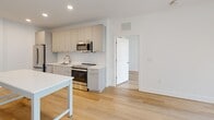 Located at 3348 W Moore St in Richmond, Virginia, this single-floor residence showcases a clean, modern design aesthetic throughout. Light hardwood flooring flows consistently across the entire unit, lending a sense of warmth and cohesion to each space.

The kitchen is a standout feature, outfitted with sleek gray flat-front cabinetry accented by gold hardware, white quartz countertops, and a classic subway tile backsplash. Stainless steel appliances — including a French door refrigerator, electric range, dishwasher, and microwave — provide a fully equipped cooking environment. Ample upper and lower cabinetry ensures generous storage throughout.

The open layout connects the kitchen to the living areas, with natural light streaming in through large windows that brighten the white-walled interiors. The bedrooms are clean and minimal, with large windows that allow for additional natural light and fresh air.

Two bathrooms serve the unit, each finished with consistent materials and attention to detail. One bathroom features a full soaking tub with a tiled surround and a sliding glass enclosure, while the second offers a glass-enclosed walk-in shower. Both bathrooms include gray vanity cabinetry with gold hardware and white countertops, complementing the overall design palette.

The unit's bright, neutral palette and modern finishes create a polished and functional living environment throughout.