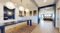 Located at 21401 Dushane Pkwy in Farmington, MN, this thoughtfully designed residential lobby offers an expansive and cohesive communal experience across a single, generously proportioned floor. The entrance greets residents with warm light wood flooring, oversized globe pendant lights suspended from brass fixtures, and a wall of crisp white mailboxes accented by wood-paneled niches and gold table lamps — creating a refined yet welcoming first impression. A bold navy console table and a vibrant patterned area rug add character to the space. The great room serves as the social centerpiece, featuring a coffered ceiling, a sleek linear fireplace, a mounted flat-screen TV, and an elegant sputnik chandelier. Comfortable seating arrangements and lush greenery enhance the inviting atmosphere. The kitchen area showcases powder-blue cabinetry with brass hardware set against a textured tile backsplash and marble countertops, complemented by curated artwork. The adjacent dining area offers a substantial wood table beneath brass pendant lighting, with a vibrant red-toned rug and a secondary yellow-green kitchenette nearby. The game room features deep blue walls, patterned wallcoverings, a distinctive multi-globe chandelier, a dedicated gaming table, and a wall-mounted TV, making it ideal for entertainment and casual gatherings.