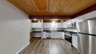 Located at 298 Northeast Ave in Tallmadge, Ohio, this single-floor, 2-bedroom, 1-bathroom home offers a distinctive architectural character defined by its signature tongue-and-groove wood plank ceilings and exposed dark wood beams throughout. The open kitchen is well-appointed with white shaker cabinetry, dark countertops, stainless steel appliances including a dishwasher, range, and microwave, and a built-in desk area — all set atop durable hardwood-style flooring. The layout flows through multiple hallways, providing a sense of connectivity, with louvered closet doors adding a classic design touch. The spacious living area is carpeted and features large sliding glass doors that invite natural light and provide outdoor access. The primary bedroom offers a generous footprint with a full closet, carpeted floors, and the same characteristic wood ceiling. The full bathroom includes a tub/shower combo, a rich wood-toned vanity with open shelving, a medicine cabinet, and hardwood-style flooring. Throughout the home, baseboard heating units are present in key areas. The cohesive use of warm wood tones across the ceilings creates a cozy, cabin-inspired ambiance across the entire living space.
