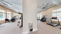 Located at 2080 Griffon Rd in Vero Beach, Florida, this well-appointed fitness center offers a generously sized, single-floor layout designed to accommodate a comprehensive range of workout activities. The main exercise area is characterized by soaring ceilings with exposed beam detailing, recessed lighting, and large-scale ceiling fans that promote airflow throughout the space. Rows of floor-to-ceiling windows line the walls, flooding the interior with natural light and providing open views of the surrounding Florida landscape.

The main floor is divided into distinct functional zones. The cardio area is equipped with ellipticals, stationary bikes, stair climbers, treadmills, and a rowing machine, all arranged along the windowed walls to maximize the sense of openness. The strength training zone features a robust selection of selectorized machines, a cable system, a power rack with weight plates, a punching bag, a full dumbbell rack, and adjustable benches. Wall-mounted televisions are positioned for easy viewing throughout.

A separate, dedicated studio room features hardwood flooring and an Xponential+ functional training station complete with suspension straps, medicine balls, kettlebells, and resistance bands — ideal for group or individual training sessions. Neutral-toned carpet in the main area, glass-paneled entry doors, and a clean, modern aesthetic give the entire facility a polished, welcoming atmosphere.