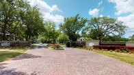 Located along Ashley River Road in Charleston, South Carolina, The Avenues is a single-story residential community distinguished by its thoughtfully designed exterior and lush natural surroundings. The entrance makes a strong first impression, featuring a wide, decorative brick paver driveway flanked by monument signage, manicured shrubs, colorful flowering plants, and dramatic red-leafed accents. Tall, mature trees provide generous shade throughout the property, creating a canopy-like atmosphere that enhances the community's sense of tranquility.

Interior roadways wind through well-maintained grounds lined with towering oaks draped in Spanish moss, lending the community a distinctly Southern coastal character. Residential buildings are clad in dark brown siding with balconies and covered entryways, set back from the roads amid open green lawns. A decorative island roundabout with a sago palm, river rock, and seasonal blooms serves as a notable focal point within the community.

A serene pond situated toward the rear of the property adds a natural amenity, with a small dock and surrounding greenery offering picturesque waterfront views. Ample surface parking is distributed throughout, shaded by the property's extensive tree canopy. The overall ambiance is quiet, verdant, and characteristic of Lowcountry living.