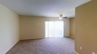 Located at 3 Fallon Ct, this single-story unit offers a straightforward, functional layout designed for comfortable everyday living. The main living area is generously sized, featuring wall-to-wall carpeting in a neutral tone that complements the warm beige walls throughout. A ceiling fan is centrally positioned overhead, providing both air circulation and a subtle lighting element to the room.

Natural light is a defining feature of this space, streaming in through a large sliding glass door fitted with sheer vertical blinds. The sliding door provides direct access to an outdoor area, offering a seamless connection between the interior living space and the exterior. The bright, airy atmosphere created by this expansive glazed opening gives the room an open and welcoming feel.

The clean, uncluttered design of the space allows for flexible furniture arrangement to suit various lifestyle needs. Neutral finishes on the walls and floors create a versatile backdrop that accommodates a range of décor styles. The overall ambiance is calm and practical, making this a well-lit, move-in ready space suitable for a variety of occupants.