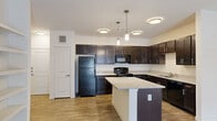 This single-floor residence offers a thoughtfully designed layout that balances functionality and modern style throughout. The kitchen serves as a standout feature, showcasing rich dark espresso cabinetry that extends to the ceiling, light granite countertops, and a central island that provides additional prep space and seating. Black appliances, including a full-size refrigerator, range, and built-in microwave, complement the cabinetry's bold tones, while pendant lighting adds a polished finishing touch overhead. The kitchen flows seamlessly into an open living area finished with warm wood-style plank flooring, creating a cohesive and inviting atmosphere. A ceiling fan overhead enhances comfort throughout the space. The bedroom is bright and airy, featuring a window with natural light, a ceiling fan, and the same wood-style flooring for a consistent aesthetic. French doors in the living area open to a private patio, offering a convenient indoor-outdoor connection. The bathroom is finished with clean white subway tile surrounding a soaking tub, light tile flooring, and crisp white walls, creating a calm and functional retreat. Neutral wall tones and clean lines throughout the unit contribute to a bright, modern, and move-in-ready living environment.