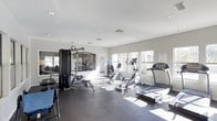 This fitness center is designed to support a comprehensive workout experience within a clean, functional layout. The space is finished with neutral gray walls and a dark rubber flooring, providing a practical and professional atmosphere suited for exercise. Recessed ceiling lights are evenly distributed throughout, ensuring consistent illumination across the entire floor.

Large windows line one wall of the facility, allowing ample natural light to stream in and offering views of the surrounding exterior. The bright, open feel of the space is further enhanced by a mirrored wall, which visually expands the room and allows users to monitor their form during workouts.

The fitness center is outfitted with a well-rounded selection of equipment. Cardio machines include a treadmill, an elliptical trainer, and a rowing machine, catering to a range of aerobic training preferences. A multi-station cable weight machine provides options for strength and resistance training, complemented by an adjustable workout bench. A water cooler station is conveniently accessible within the space. Safety and facility information is posted on the walls, ensuring users have easy access to guidelines. The single-floor layout keeps everything accessible and easy to navigate.