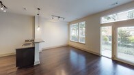 This thoughtfully designed single-floor residence offers a cohesive blend of modern finishes and functional layout. The kitchen is a standout feature, showcasing dark espresso cabinetry that extends to the ceiling for ample storage, granite countertops with subtle natural veining, a classic white subway tile backsplash, and a full suite of stainless steel Whirlpool appliances including a side-by-side refrigerator with ice and water dispenser, electric range, built-in microwave, and dishwasher. Rich hardwood flooring runs throughout the kitchen and living areas, adding warmth and continuity to the space. The open living area is generously proportioned, bathed in natural light streaming through large windows with views of lush greenery. Pendant lighting and track lighting add both ambiance and practicality. A breakfast bar connects the kitchen to the living space, enhancing the open-concept feel. The bathroom is finished with neutral tile flooring and a tile-surround soaking tub and shower combination, complemented by a dark-cabinetry vanity, framed mirror, and an overhead storage cabinet, creating a clean and functional retreat. The overall aesthetic is contemporary and polished throughout.