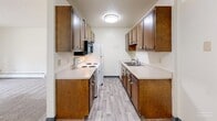 Located at 3401 E 11th St in Sioux Falls, SD, this one-bedroom, one-bathroom unit offers a practical and well-organized single-floor layout. The open-concept living and dining area is carpeted and bathed in natural light from a sliding glass door that leads to an outdoor green space, creating a bright and inviting atmosphere. A ceiling fan adds comfort to the living area, which also features baseboard heating. The galley-style kitchen is efficiently designed with rich, dark-stained wood cabinetry lining both walls, light countertops, a double-basin sink, and white appliances including an electric range and refrigerator, all set on wood-look hard flooring. The bedroom is a comfortable, carpeted space featuring its own ceiling fan, a large window with vertical blinds, and baseboard heating, providing a quiet and functional retreat. Three closets throughout the unit offer generous storage. The full bathroom is clean and straightforward, featuring a tub/shower combo with white surround, wood-look flooring, and crisp white fixtures. Textured ceilings and warm wood-toned doors and trim are consistent throughout, lending the space a cohesive, classic character.