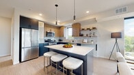 This thoughtfully designed single-floor residence showcases a contemporary aesthetic throughout its well-laid-out floor plan. The kitchen serves as a centerpiece, featuring striking two-tone cabinetry that pairs navy lower cabinets with warm wood-finish uppers, all complemented by crisp white quartz countertops and a subtle tile backsplash. A central island with seating provides additional prep space and casual dining, while stainless steel appliances, open shelving, and light wood-style flooring complete the polished look.

The living area is bright and airy, benefiting from floor-to-ceiling windows and a sliding glass door that opens onto a private balcony with outdoor views of surrounding greenery. This seamless indoor-outdoor connection creates an inviting, open atmosphere throughout the main living space.

Two bedrooms feature plush carpeting and generous windows that bring in natural light and treetop views, lending each room a calm and comfortable character. The primary bedroom includes a dedicated en-suite bathroom with a walk-in shower, dark vanity cabinetry, and wood-look flooring. A second full bathroom with a shower-tub combination mirrors the same modern, clean finishes found throughout the unit.