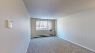 Located at 4920 Thunderbird Circle in Boulder, Colorado, this one-bedroom, one-bathroom unit offers a thoughtfully organized single-floor layout that makes efficient use of its compact footprint. The living area is finished with plush carpeting and neutral-toned walls, creating a clean and versatile space. A large window with vertical blinds allows natural light to fill the room, and a baseboard heating unit runs along the wall, ensuring year-round comfort. The galley-style kitchen is a standout feature, showcasing dark espresso cabinetry, light countertops, a double-basin sink, and a full suite of black appliances including a refrigerator, electric range, and built-in microwave. Stone-tile flooring grounds the kitchen with a warm, durable finish. The bedroom is a well-proportioned retreat with soft carpeting, a dedicated closet with a rod and shelf for organized storage, and its own window that brings in natural light. A second closet provides additional storage elsewhere in the unit. The bathroom is finished with full-height white ceramic tile surrounding a soaking tub and shower combination, accented by a classic brown tile border. A wall-mounted light fixture illuminates the entryway corridor, connecting the spaces with a functional and welcoming flow throughout the unit.