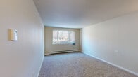 Located at 4920 Thunderbird Circle in Boulder, Colorado, this one-bedroom, one-bathroom unit offers a thoughtfully organized single-floor layout that makes efficient use of its compact footprint. The living area is finished with plush carpeting and neutral-toned walls, creating a clean and versatile space. A large window with vertical blinds allows natural light to fill the room, and a baseboard heating unit runs along the wall, ensuring year-round comfort. The galley-style kitchen is a standout feature, showcasing dark espresso cabinetry, light countertops, a double-basin sink, and a full suite of black appliances including a refrigerator, electric range, and built-in microwave. Stone-tile flooring grounds the kitchen with a warm, durable finish. The bedroom is a well-proportioned retreat with soft carpeting, a dedicated closet with a rod and shelf for organized storage, and its own window that brings in natural light. A second closet provides additional storage elsewhere in the unit. The bathroom is finished with full-height white ceramic tile surrounding a soaking tub and shower combination, accented by a classic brown tile border. A wall-mounted light fixture illuminates the entryway corridor, connecting the spaces with a functional and welcoming flow throughout the unit.