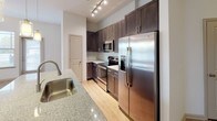 This well-appointed 3-bedroom, 2-bathroom single-story residence offers a thoughtfully designed open-concept layout. The main living and dining area is bathed in natural light from a row of windows, complemented by wood-look flooring and a ceiling fan overhead. The kitchen is outfitted with dark espresso cabinetry reaching near the ceiling, granite-style countertops, a subway tile backsplash, and a full suite of stainless steel appliances including a refrigerator with ice maker, electric range, and microwave. A kitchen island with pendant lighting and an undermount sink adds both function and style, flowing seamlessly into the living space. The primary bedroom features plush carpeting, an elevated ceiling with a ceiling fan, and access to a spacious walk-in closet with multi-tier wire shelving. The ensuite primary bathroom includes a lengthy double-sink vanity with granite countertops, dark cabinetry, a separate glass-enclosed shower with tile surround, and a private water closet. The two secondary bedrooms are carpeted and include ceiling fans and natural light from windows. The second bathroom offers a tiled tub-shower combo, granite vanity, and wood-look flooring throughout.