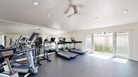 Located at 6312 Birdcage St in Citrus Heights, CA, this fitness center offers a well-organized and fully equipped exercise space designed to support a wide range of workout routines. The room features clean white walls, a smooth white ceiling with recessed lighting, and durable rubber flooring that provides comfort and traction throughout the workout area. A ceiling fan helps maintain air circulation, while a wall-mounted HVAC unit ensures climate control year-round. Large windows and glass French doors flood the space with natural light and offer views of the surrounding greenery, creating an open and inviting atmosphere. The cardio section is equipped with multiple treadmills and a recumbent bike, complemented by a large mirrored wall that enhances the sense of space. The strength and free weights area includes a full dumbbell rack, medicine balls, resistance bands, foam rollers, adjustable benches, and a multi-function cable machine. A water fountain is conveniently situated within the room for easy access during workouts. The overall ambiance is clean, modern, and functional, providing residents with a comprehensive fitness facility that accommodates both cardio and strength training needs in a bright, well-maintained environment.