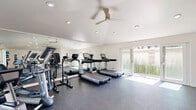 Located at 6312 Birdcage St in Citrus Heights, CA, this fitness center offers a well-organized and fully equipped exercise space designed to support a wide range of workout routines. The room features clean white walls, a smooth white ceiling with recessed lighting, and durable rubber flooring that provides comfort and traction throughout the workout area. A ceiling fan helps maintain air circulation, while a wall-mounted HVAC unit ensures climate control year-round. Large windows and glass French doors flood the space with natural light and offer views of the surrounding greenery, creating an open and inviting atmosphere. The cardio section is equipped with multiple treadmills and a recumbent bike, complemented by a large mirrored wall that enhances the sense of space. The strength and free weights area includes a full dumbbell rack, medicine balls, resistance bands, foam rollers, adjustable benches, and a multi-function cable machine. A water fountain is conveniently situated within the room for easy access during workouts. The overall ambiance is clean, modern, and functional, providing residents with a comprehensive fitness facility that accommodates both cardio and strength training needs in a bright, well-maintained environment.