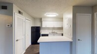 This single-floor unit offers a practical and clean layout designed for comfortable everyday living. The kitchen is a central highlight, featuring crisp white upper cabinetry that provides ample storage, a white countertop peninsula that offers additional workspace and casual dining potential, and a full suite of black appliances including a refrigerator, dishwasher, and range. A stainless steel sink is positioned along the back wall beneath the cabinetry, and a louvered closet door nearby adds convenient storage. Flush-mount ceiling lighting illuminates the space, and a textured ceiling is consistent throughout the unit.

The remaining rooms share a cohesive aesthetic defined by dark hardwood-style flooring, neutral warm-toned walls with clean white baseboards, and textured ceilings. Each room is served by a flush-mount light fixture and features at least one window fitted with horizontal blinds, allowing natural light to filter in while maintaining privacy. The windows offer views of the surrounding exterior environment. The open, unfurnished layout of these rooms provides flexibility for a variety of uses, whether as living areas, bedrooms, or dedicated workspaces. Overall, the unit presents a tidy, functional aesthetic with consistent finishes throughout.