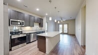 Located in San Marcos, TX, this well-appointed 3-bedroom, 3-bathroom residence on a single floor offers a thoughtfully designed layout with modern finishes throughout. The open-concept kitchen serves as the heart of the home, showcasing dark espresso cabinetry, granite countertops, a full suite of stainless steel appliances including a French door refrigerator, gas range, built-in microwave, and dishwasher. A large central island with pendant lighting provides additional prep space and casual seating, flowing seamlessly into the living area. Wood-look plank flooring extends throughout the entire residence, lending warmth and continuity to each room. The bedrooms are bright and comfortable, with large windows that invite natural light and offer views of the surrounding neighborhood. Ceiling fans add to the functional comfort of the living spaces. Each of the three bathrooms is outfitted with dark cabinetry, granite vanity countertops, and tub-shower combinations. The primary bathroom features a dual-sink vanity for added convenience. A walk-in closet with wire shelving provides generous storage. Panel-style interior doors and neutral wall tones give the space a clean, contemporary feel throughout.