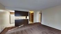 Located at 6175 Northgate Rd in Columbus, Ohio, this single-floor residence offers a practical and functional layout designed for comfortable everyday living. The open-concept design connects the kitchen and living area seamlessly, creating a spacious and cohesive environment. The kitchen is equipped with dark cabinetry, a built-in stovetop, a sink, and a refrigerator, all framed by a peninsula counter that separates it from the main living space. The flooring transitions from hard surface in the kitchen to wall-to-wall carpeting in the living area, adding warmth underfoot. White walls throughout the unit keep the interior bright and neutral. A hallway extends from the living area, leading to additional rooms, and features louvered closet doors that provide convenient storage access. Multiple doorways are visible, suggesting well-distributed room connections throughout the unit. Natural light filters into the living area, contributing to an open and airy feel. The overall layout is straightforward and efficient, making it a practical choice for those seeking a well-organized, single-level living space in the Northgate area of Columbus.