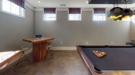 Located at 105 Exchange Dr in Asheville, NC, this single-floor space is designed as a dedicated entertainment and recreation area. The layout is open and well-proportioned, centered around a full-size pool table with a rich wood frame and dark felt surface, accompanied by a dedicated cue rack nearby. Billiards-themed artwork adorns one wall, adding a cohesive, purposeful aesthetic to the space.

Polished concrete floors run throughout, providing a durable and modern foundation that reflects natural light streaming in through a row of horizontal windows dressed with deep burgundy Roman shades. The neutral gray walls and crisp white crown molding and baseboards create a clean, contemporary backdrop.

A standout feature is the live-edge wood bar table paired with industrial-style stools, positioned beneath a wall-mounted flat-screen TV — making the space equally suited for gathering and watching events. A set of glass-paned French doors with white trim connects this room to an adjacent area, offering transparency and an elegant transition between spaces. Recessed lighting complements the natural light, ensuring the room is well-lit throughout the day. Overall, the space strikes a balance between recreational functionality and refined design.