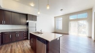 This single-floor residence is designed with a contemporary open-concept layout that seamlessly connects the kitchen and living areas. The kitchen serves as a central hub, anchored by a large island with a double-basin sink, granite-style countertops, and pendant lighting overhead. Dark espresso cabinetry extends floor-to-ceiling, providing ample storage, while stainless steel appliances — including a refrigerator, microwave, and range — add a polished, modern aesthetic. Hardwood-style flooring runs throughout the main living areas, contributing warmth and visual continuity.

The living area is bright and open, benefiting from large windows and a sliding glass door that invites natural light and provides access to an outdoor space. The bedroom features plush carpeting and a well-positioned window that further enhances the sense of openness.

The bathroom is finished with large-format tile flooring, dark cabinetry with granite-style countertops, and a tub-shower combination, maintaining the consistent design language found throughout the unit. Overall, the space presents a clean, modern aesthetic with cohesive finishes and thoughtful design details.