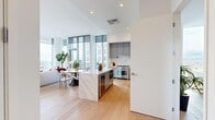 This thoughtfully designed high-rise residence offers a seamless blend of modern luxury and functional living across a single, well-appointed floor. The open-plan kitchen and living area serves as the heart of the home, anchored by dramatic floor-to-ceiling windows that frame sweeping panoramic city skyline views and flood the space with natural light. Light oak hardwood flooring runs throughout, adding warmth against the crisp white palette.

The gourmet kitchen is outfitted with custom slate-gray cabinetry, a striking marble-veined waterfall island with an integrated wine cooler, a professional-grade stainless steel range, and a full-height panel-ready refrigerator. The open living and dining area benefits from soaring ceilings and expansive glazing with direct balcony access.

The generously sized primary bedroom features elevated ceilings, warm wood tones, and access to two well-organized walk-in closets with custom built-in shelving. The primary bathroom is a standout, showcasing full-slab marble wall cladding, a freestanding soaking tub, a glass-enclosed rainfall shower, and refined stone tile flooring. A second full bathroom and a dedicated home office — with its own breathtaking city views — round out this exceptional residence.