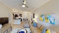 Located at 1415 E NC-54 Hwy in Durham, North Carolina, this single-floor residence offers a thoughtfully designed open-concept layout that seamlessly connects the main living areas. The living room is a welcoming, well-lit space featuring crown molding, a ceiling fan with a light fixture, and smooth, neutral-toned walls that create a warm and inviting ambiance. Light hardwood flooring runs throughout, adding continuity and a sense of spaciousness to the open floor plan. The kitchen is equipped with dark cabinetry, stainless steel appliances, and a kitchen island with a light-colored countertop that doubles as a breakfast bar, complemented by pendant lighting overhead. A dedicated dining area sits adjacent to the kitchen, furnished with a round table and chairs, ideal for everyday meals or casual gatherings. Recessed track lighting in the kitchen and pendant fixtures throughout enhance the functionality and aesthetic of the space. Crown molding details are consistent across the living areas, adding a refined architectural touch. The overall design balances modern finishes with comfortable, livable interiors, making this a practical and attractive single-story home in the Durham area.