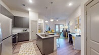 This single-floor residence offers a thoughtfully designed open-concept layout that seamlessly connects the kitchen, dining, and living areas. The kitchen is a standout feature, equipped with stainless steel appliances including a refrigerator, range, and microwave, complemented by granite countertops, a subway tile backsplash, and sleek gray cabinetry. A central island with a built-in sink and pendant lighting above serves as both a functional workspace and a casual dining spot with bar seating. Light wood-style flooring flows throughout, enhancing the bright, airy atmosphere created by recessed lighting and a ceiling fan. The living area is generously sized, offering access to the outdoors through double French doors that bring in natural light and exterior views. A built-in desk area provides a convenient workspace within the main living space. The bedroom is a comfortable retreat, featuring a large window with views, a ceiling fan, and ample room for a full furniture arrangement. The bathroom is well-finished with a granite-topped vanity, gray cabinetry, a large mirror, and wood-style flooring. Throughout the space, a cohesive modern aesthetic is maintained with clean lines, neutral walls, and contemporary fixtures.