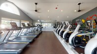 Located at 1647 Westminster Dr in Naperville, IL, this Athletic Club fitness center is a well-equipped, single-floor facility designed to support a comprehensive workout experience. The space is organized into distinct workout zones, each thoughtfully appointed with quality equipment and motivating design elements.

The main cardio floor features a generous row of treadmills and elliptical machines positioned beneath vaulted ceilings with recessed lighting and ceiling fans. Large sliding windows and glass doors along one wall flood the space with natural light and offer direct views of an outdoor pool and patio area, creating an open, airy atmosphere.

The strength training zone is anchored by a full rack of dumbbells, a cable machine, and various resistance equipment, all set against a dramatic dark accent wall bearing an inspirational quote. Full-length mirrors amplify the sense of space and allow for proper form checks during workouts.

A dedicated functional fitness area houses stability balls, medicine balls, foam rollers, and additional accessories neatly organized in a white modular storage unit. This section also includes a wall-mounted water fountain for convenience. Durable rubber flooring throughout provides safety and comfort underfoot.

The facility's cool gray and dark teal color palette, combined with motivational wall graphics and the "Athletic Club" branding, contributes to an energetic and professional ambiance suited for serious fitness pursuits.