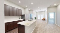 Located in Conroe, TX, this single-floor, 2-bedroom, 3-bathroom residence offers a thoughtfully designed layout that balances functionality and modern style. The open-concept kitchen and living area serves as the heart of the home, featuring rich dark espresso cabinetry, crisp white quartz countertops, and stainless steel appliances, including a range, microwave, and refrigerator. A central kitchen island with a built-in sink provides additional workspace and flows seamlessly into the carpeted living area, which is brightened by recessed lighting and French doors that invite natural light. The primary bedroom is a comfortable retreat with plush carpet, vaulted ceilings, and direct access to a private en-suite bathroom. The en-suite boasts a dual-sink vanity with dark cabinetry, white countertops, hardwood-style flooring, and a walk-in closet with built-in shelving and hanging rods. The secondary bedroom is equally well-sized, also carpeted, with a double-door closet and convenient access to an adjacent bathroom. A spacious living area with recessed lighting and neutral tones throughout creates a clean, contemporary ambiance. The consistent use of dark wood cabinetry and white countertops across the kitchen and bathrooms lends the space a cohesive, polished aesthetic.
