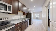 Located at 4750 Innovation Dr., Unit #117 in Lincoln, Nebraska, this studio unit offers a thoughtfully designed single-floor layout that maximizes every square foot. Light-toned hardwood-style flooring flows seamlessly throughout, giving the space a clean, cohesive look.

The kitchen is well-appointed with rich dark espresso cabinetry featuring brushed nickel hardware, granite countertops, a stainless steel refrigerator, range with microwave above, dishwasher, and a deep single-basin sink with a modern pull-down faucet — all illuminated by recessed lighting overhead.

The open living area is bright and airy, benefiting from natural light through a large window and a sliding glass door that leads directly to a ground-floor patio with outdoor views. A wall-mounted HVAC unit provides convenient climate control.

The bathroom mirrors the kitchen's design aesthetic, featuring matching dark cabinetry, granite countertops, a large vanity mirror, and a glass-enclosed shower stall with light tile flooring.

A dedicated laundry area houses a full-size side-by-side washer and dryer with overhead shelving for added storage. A separate closet provides additional organization. Neutral wall tones and recessed lighting throughout contribute to the unit's modern, move-in-ready appeal.