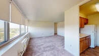This single-floor unit at 2400 McClellan Ave in Pennsauken, New Jersey, offers a clean, well-lit interior defined by a neutral color palette of crisp whites and soft warm tones throughout. The layout flows naturally from a carpeted hallway connecting the main living areas, with each room benefiting from consistent plush gray carpeting that adds comfort underfoot.

The spacious living area is a standout feature, showcasing a wide bank of multiple windows fitted with roller shades that flood the room with natural light while framing scenic treetop and neighborhood views. A wall-mounted air conditioning unit and baseboard heating ensure year-round climate control. The open, airy feel of this room makes it well-suited for a variety of furniture arrangements.

An additional carpeted room, accessible via the living area, offers similar window placement and views, along with its own wall unit and baseboard heating, providing flexible use as a bedroom or secondary living space.

The galley-style kitchen features warm oak cabinetry, white appliances including a gas range and full-size refrigerator, light countertops, and tile flooring — providing a practical and efficient cooking space.

The bathroom is finished with small-format tile flooring, a vanity with dark countertop and white cabinetry, and a separate tub and toilet area, offering a functional and tidy design.