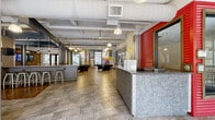 This dynamic amenity floor showcases a thoughtfully designed communal space that blends industrial aesthetics with vibrant, energetic décor. The welcoming lobby greets residents with a sleek galvanized metal reception desk, pendant lighting, and large-format tile flooring that carries throughout much of the level. Exposed beams, ductwork, and structural steel columns lend an industrial character to the open lounge and social hub, which features a wood-topped bar with barstool seating, integrated cabinetry, flat-screen TVs, and comfortable lounge furniture — all beneath soaring, exposed ceilings.

A game room area adds a lively touch with a pool table and bold, colorful wall murals, while vending stations provide added convenience. Floor-to-ceiling windows in the pool-view lounge flood the space with natural light and offer sweeping views of the outdoor pool deck. This area is appointed with high-top tables and stools for casual gathering.

The well-equipped fitness center features a rubberized floor in contrasting yellow and grey tones, a comprehensive selection of cardio and strength machines, ceiling fans, and wall-mounted TVs. Wide, generously lit corridors with cheerful yellow, teal, and blue accent walls connect the various amenity spaces, creating a cohesive and navigable layout throughout the floor.