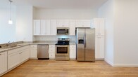 Located at 30 Veterans Memorial Pkwy in East Providence, Rhode Island, this single-floor unit offers a clean, contemporary design with an emphasis on functionality and modern finishes throughout. Light-toned hardwood flooring flows consistently through the main living areas, complementing the crisp white walls and recessed lighting that create a bright, welcoming atmosphere.

The open-concept living area connects seamlessly to the kitchen, which serves as a standout feature of the space. The kitchen is appointed with white shaker-style cabinetry, granite countertops, a deep stainless steel sink, and a full suite of stainless steel appliances including a refrigerator with ice maker, electric range, microwave, and dishwasher. Pendant lighting adds a refined touch above the kitchen counter.

The bedrooms are generously proportioned, each featuring light hardwood floors, recessed lighting, and large windows that invite abundant natural light. One bedroom includes glass doors that open to an outdoor balcony area, enhancing the sense of connection to the exterior.

The bathrooms are finished with granite-topped white vanities, chrome fixtures, and clean white surrounds. A dedicated laundry area houses a stacked washer and dryer unit alongside additional cabinetry with a granite countertop. The overall design is cohesive, modern, and move-in ready.