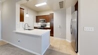 This single-story, one-bedroom, one-bathroom residence offers a thoughtfully designed open-concept layout that maximizes its comfortable footprint. The living room is finished with plush carpet, crown molding, and a ceiling fan, while track lighting adds a modern touch. A large glass door opens to an outdoor area, allowing natural light to fill the space. The kitchen is accessible via a pass-through peninsula with a white countertop, creating seamless connectivity to the living area. Inside, the kitchen features rich dark wood cabinetry, a classic white subway tile backsplash, light tile flooring, stainless steel appliances including a refrigerator, electric range, and built-in microwave, plus a full-sized pantry enclosed by double doors. The bedroom is generously sized, carpeted, and highlighted by a striking arched window that frames outdoor views, complemented by a ceiling fan. It connects directly to a spacious walk-in closet outfitted with multi-tiered wire shelving and hanging rods. The bathroom includes a dark wood vanity with a white countertop, tile flooring, and a glass-enclosed walk-in shower with tile surround, offering a clean, functional design throughout.