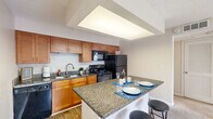 Located at 100 Lakeshore Crossing NE in Atlanta, Georgia, this one-bedroom, one-bathroom residence offers a well-organized single-floor layout designed for comfortable everyday living. The kitchen is a standout feature, showcasing warm honey-toned cabinetry, dark granite countertops, hardwood-style flooring, and a full suite of black appliances including a dishwasher, range, microwave, and refrigerator. A recessed ceiling detail with integrated lighting adds architectural interest above the kitchen. A granite-topped peninsula extends from the kitchen, providing bar-style seating and serving as a natural divider between the kitchen and living area — ideal for dining or casual entertaining. The living area benefits from a sliding glass door that draws in natural light and connects to the outdoors. The bedroom is generously proportioned, finished with plush wall-to-wall carpeting, neutral tones, and a ceiling fan with light fixture. A large window frames outdoor views, enhancing the sense of brightness and openness. The bathroom includes a walk-in glass-door shower, wood-style flooring, and a granite vanity with matching cabinetry. A stacked washer and dryer unit is conveniently located adjacent to the bathroom, adding practical in-unit laundry access. A dedicated closet and hallway complete the efficient, functional floor plan.