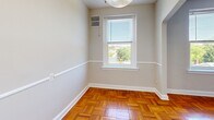 Located on the fourth floor at 6817 Georgia Ave NW in Washington, DC, Unit 405 is a well-appointed one-bedroom, one-bathroom residence that makes efficient use of its space. Throughout the living and bedroom areas, warm-toned parquet hardwood flooring in a classic basket-weave pattern adds character and a timeless aesthetic to every room.

The open living and dining area is brightened by natural light streaming through large windows that offer tree-lined views of the surrounding neighborhood. A ceiling fan overhead provides added comfort, while neutral gray walls create a clean, versatile backdrop. An elegant arched doorway connects the living area to the rest of the unit, adding an architectural charm.

The generously sized bedroom features the same distinctive parquet flooring, large windows with outdoor views, a ceiling fan, and a sizable closet, providing ample storage.

The galley-style kitchen is outfitted with warm wood cabinetry, dark granite-style countertops, a gas range, stainless steel sink, and a full-size refrigerator — offering a practical and well-equipped cooking space.

The bathroom is clean and functional, featuring a white vanity with a single-basin sink, a mirror, and a full shower-tub combination with white tile surround and a curtain rod. Light tile flooring completes the crisp, bright finish of the space.