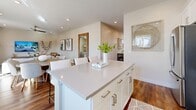 This well-appointed three-story home offers generous living space across three distinct floors, accommodating five bedrooms and four bathrooms. The main living level features an open-concept layout that seamlessly connects the kitchen, dining area, and living room. The kitchen is outfitted with white shaker cabinetry, a gray subway tile backsplash, stainless steel appliances including a gas range and built-in microwave, and a large island — all set atop warm hardwood-style flooring. The adjacent dining area benefits from natural light streaming through sliding glass doors that open to an outdoor space, while the living room offers a relaxed, airy atmosphere. Hallways throughout the home are bright and clean, with recessed lighting guiding the way between floors via three staircases. The bedrooms are comfortably sized, with the primary suite featuring its own well-organized walk-in closet with built-in shelving and a private ensuite bathroom complete with a glass-enclosed walk-in shower and a vanity with stone countertops. Additional bedrooms are well-lit with natural light. A dedicated laundry room houses a full-size washer and dryer. Four closets provide ample storage throughout. The home's consistent use of hardwood-style flooring and a neutral color palette create a cohesive, modern aesthetic.