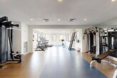 Located at 4221 E Ray Rd in Phoenix, AZ, this fitness center offers a generously sized, single-floor exercise room designed to support a wide range of workout routines. The space features a clean, modern aesthetic with bright white walls, recessed lighting, and large windows along multiple walls that invite natural light and provide open views of the surrounding landscape.

The flooring transitions between durable cork and blue rubberized surfaces, delineating distinct workout zones throughout the room. The cardio section is well-stocked with treadmills, ellipticals, stationary bikes, and a stair climber, all arranged to maximize space and accessibility. A dedicated strength training area includes a multi-station cable machine, a punching bag, resistance bands, stability balls, and a flat bench, offering a comprehensive free-weight and functional training setup. A dumbbell rack and additional benches round out the strength zone.

A standout feature is a vivid floor-to-ceiling mural depicting a classic Arizona desert landscape with saguaro cacti and wildflowers, adding a distinctive local character to the space. Mirrored wall panels enhance the sense of depth and openness. The layout is thoughtfully organized, providing ample open floor space for stretching or floor exercises. The overall ambiance is bright, clean, and motivating — well-suited for a full-spectrum fitness experience.
