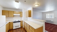 Located at 560 Adams Ave in Orange Cove, CA, this one-bedroom, one-bathroom unit offers a practical and well-organized single-floor layout. The kitchen is a standout functional space, featuring warm oak cabinetry — both upper and lower — expansive light-colored countertops, a coil-top electric range, a full-size refrigerator, an under-cabinet range hood, and a stainless steel sink positioned beneath a window that brings in natural light. Dark hardwood-style flooring runs throughout the kitchen, adding warmth and contrast to the white walls and bright counters. The bedroom is a comfortable, carpeted retreat with rich burgundy carpet, white walls, a wall-mounted HVAC unit, and a window dressed with vertical blinds that allows in ample natural light. Three closets provide generous storage throughout the unit. The bathroom includes a wood-vanity with integrated sink and countertop, a large mirror, a combination tub and shower, and a window for ventilation and light. Dark hardwood-style flooring continues here, complementing the clean white fixtures. A balcony extends the living space outdoors. The overall ambiance is clean, functional, and well-lit, with consistent warm wood tones throughout.
