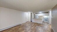 Located at 7645 SW Bonita Rd in Tigard, Oregon, this one-bedroom, one-bathroom unit offers a practical and well-organized single-floor layout. The living room is bright and open, featuring wood-style flooring, a baseboard heating system, and a sliding glass door with vertical blinds that opens onto a private balcony with outdoor views of surrounding greenery. The combined kitchen and dining area is efficiently designed with white cabinetry, light stone-finish countertops, a kitchen island with bar overhang, and white appliances including a refrigerator, electric range, and dishwasher. An adjacent pantry provides open shelving for additional storage. The bedroom is carpeted and generously sized, filled with natural light from a window overlooking mature trees, and includes access to closet space. The hallway connects the main living areas and includes multiple closets, offering notable storage capacity throughout. The bathroom features wood-style flooring, a vanity with stone-finish countertop, and a tub-shower combination. Textured ceilings are consistent throughout the unit. The overall design is clean, neutral, and functional, making efficient use of the available floor space.