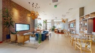 Located at 2 Harbor Point Rd S in Stamford, CT, Anthem at Harbor Point offers a thoughtfully designed amenity level that blends contemporary style with inviting, functional spaces. The expansive main lounge anchors the floor, featuring an exposed brick accent wall, a large flat-screen TV, and an eclectic mix of seating including a bold blue sofa, woven rattan chairs, and layered area rugs — all illuminated by clusters of woven pendant lights overhead. Large windows and glass walls throughout flood the space with natural light and frame views of the surrounding Harbor Point development. A dedicated dining area features a round wood table beneath artisan pendant fixtures, with sliding glass doors opening directly to an outdoor terrace. A cozy nook with a built-in white shelving unit, orange accent wall, and cushioned bench seating provides a refined reading or social retreat. The fitness center, branded with the Anthem name, is accessible via glass double doors and is equipped with a full range of exercise equipment. A serene corridor features a textured wave-pattern wall, a living green installation, and a reflective water feature. A relaxation lounge with floor-to-ceiling windows, pebble-textured flooring, and hanging hammock chairs completes this well-appointed amenity experience.
