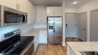 Located at 1315 Harding Pl in Charlotte's vibrant 28204 zip code, this single-floor residence offers a thoughtfully designed layout with modern finishes at every turn. The kitchen is a standout feature, showcasing white shaker-style cabinetry, light granite countertops, a classic subway tile backsplash, and a full suite of stainless steel appliances including a range, over-the-range microwave, and a side-by-side refrigerator with ice and water dispenser. Warm hardwood-style flooring anchors the kitchen and main living areas. The bedrooms are carpeted for comfort and are bathed in natural light through large windows with city and treetop views. Ceiling fans provide added comfort in the sleeping quarters. Storage is well-addressed with a generously sized walk-in closet outfitted with built-in shelving, hanging rods, and dedicated shelf towers. The primary bathroom is particularly impressive, offering a double-sink vanity with dark granite countertops, a frameless glass walk-in shower with floor-to-ceiling tile, and direct access to the walk-in closet. A secondary bathroom features a soaking tub and additional vanity storage. Light tile flooring in the bathrooms completes the clean, contemporary aesthetic throughout this well-appointed Charlotte residence.