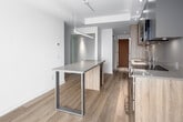 Located at 131 Mill St, unit 2611 is a thoughtfully designed one-bedroom, one-bathroom residence that makes efficient use of its compact footprint across a single floor. Light hardwood flooring runs throughout, lending warmth and continuity to the space.

The open-concept kitchen is a standout feature, equipped with stainless steel appliances including a full-size refrigerator, electric range with oven, and built-in microwave. Two-tone cabinetry pairs natural wood lower cabinets with sleek matte grey uppers, complemented by a neutral countertop and an undermount sink. A freestanding island with a slim metal frame provides additional prep and dining space, doubling as a functional centerpiece.

The living area receives generous natural light through large floor-to-ceiling windows that offer elevated outdoor views. Recessed and pendant lighting enhance the bright, airy ambiance throughout.

The bedroom is a serene, minimalist retreat featuring clean white walls and elegant sliding panel doors that maximize space efficiency. The bathroom is finished with large-format light grey tiles surrounding a soaking tub with an integrated shower system, accented by warm wood-tone detailing.

A hallway with built-in storage connects the rooms seamlessly. The overall design is modern and cohesive, with a neutral palette and quality finishes throughout.